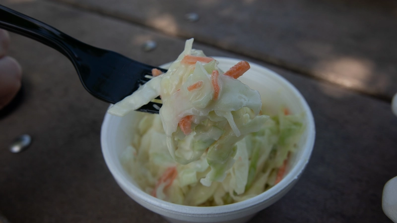 A cup of coleslaw with a plastic fork in it. 