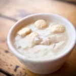 A photo of a cup of dairy free seafood chowder on a wooden table.