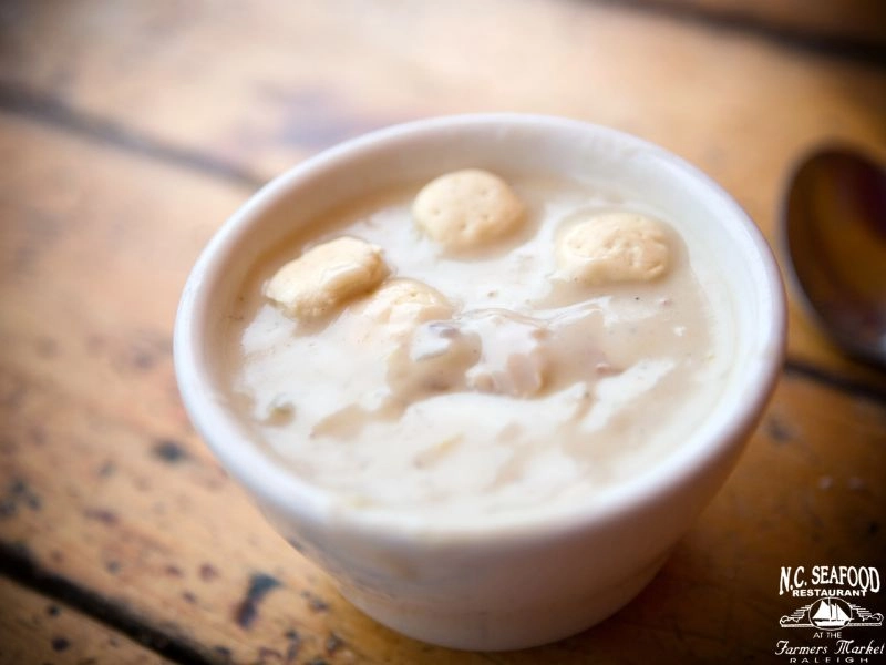 A photo of a cup of dairy free seafood chowder on a wooden table.